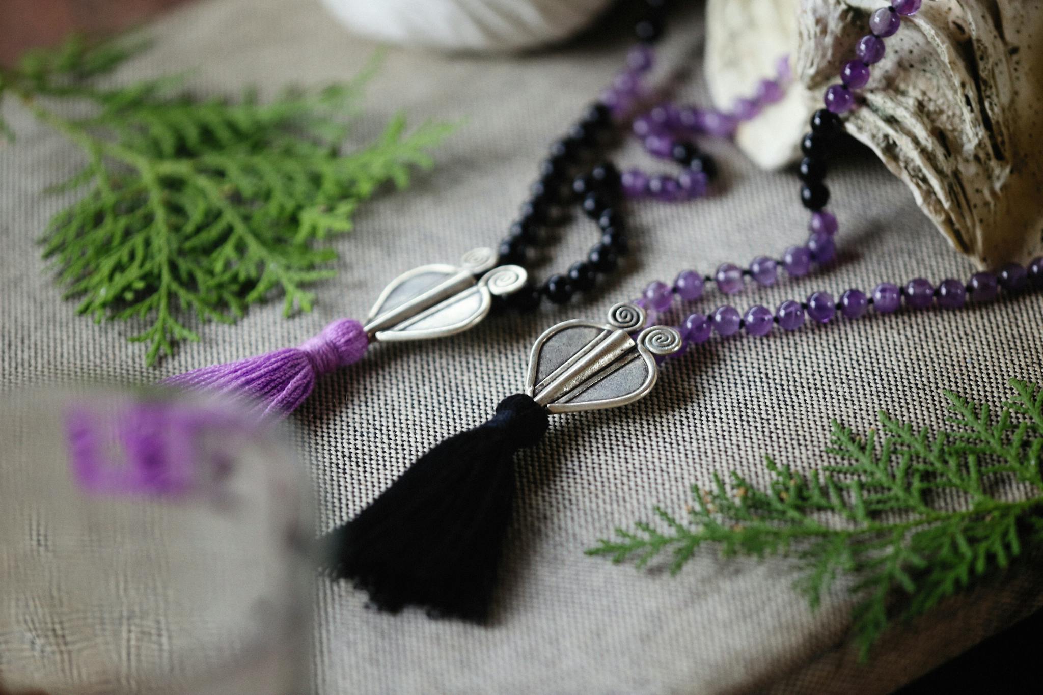 Close-up of artistic prayer beads with tassels, resting on textured fabric and greenery.