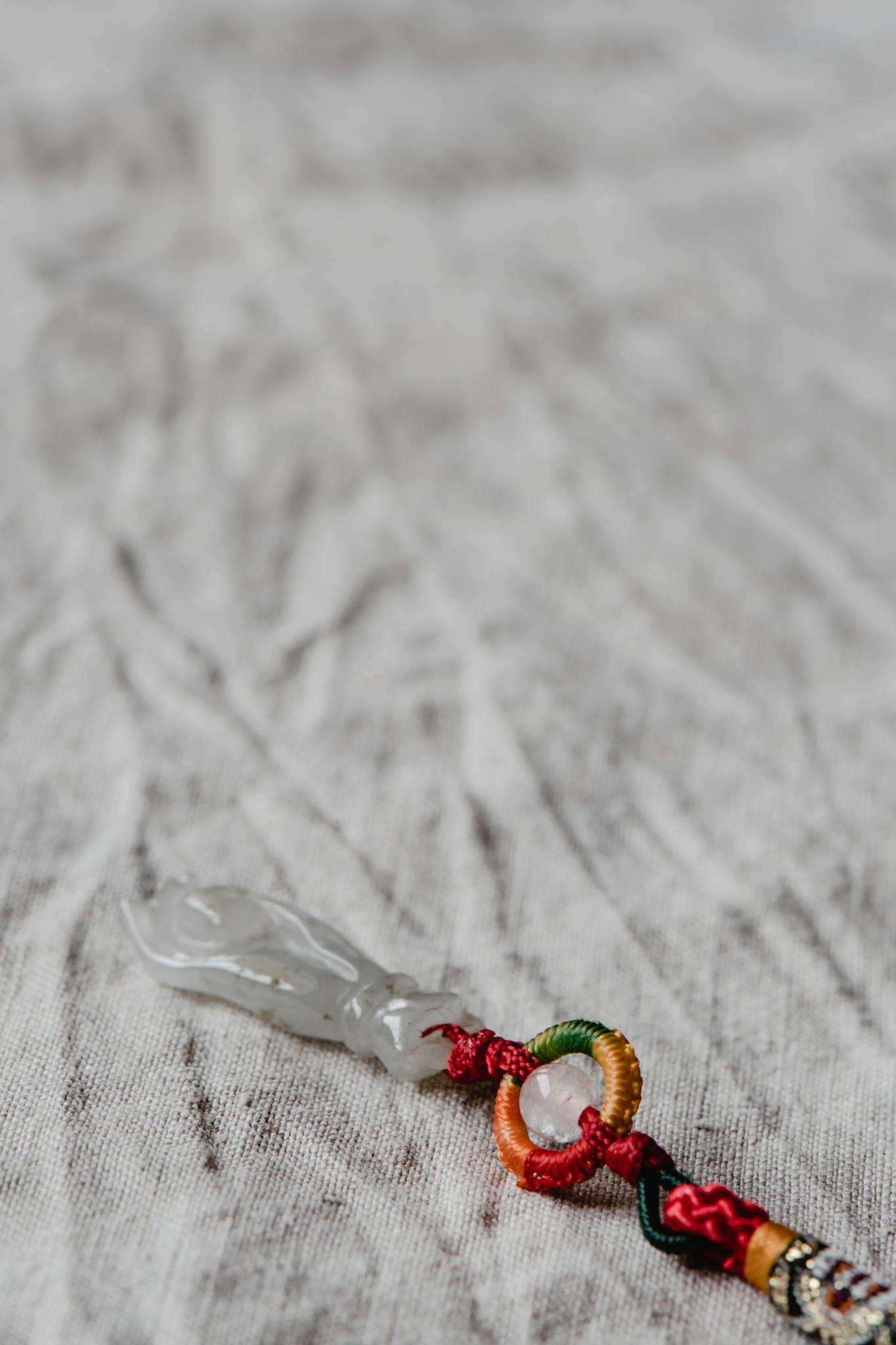 Intricate jade amulet with colorful knots on textured fabric background.